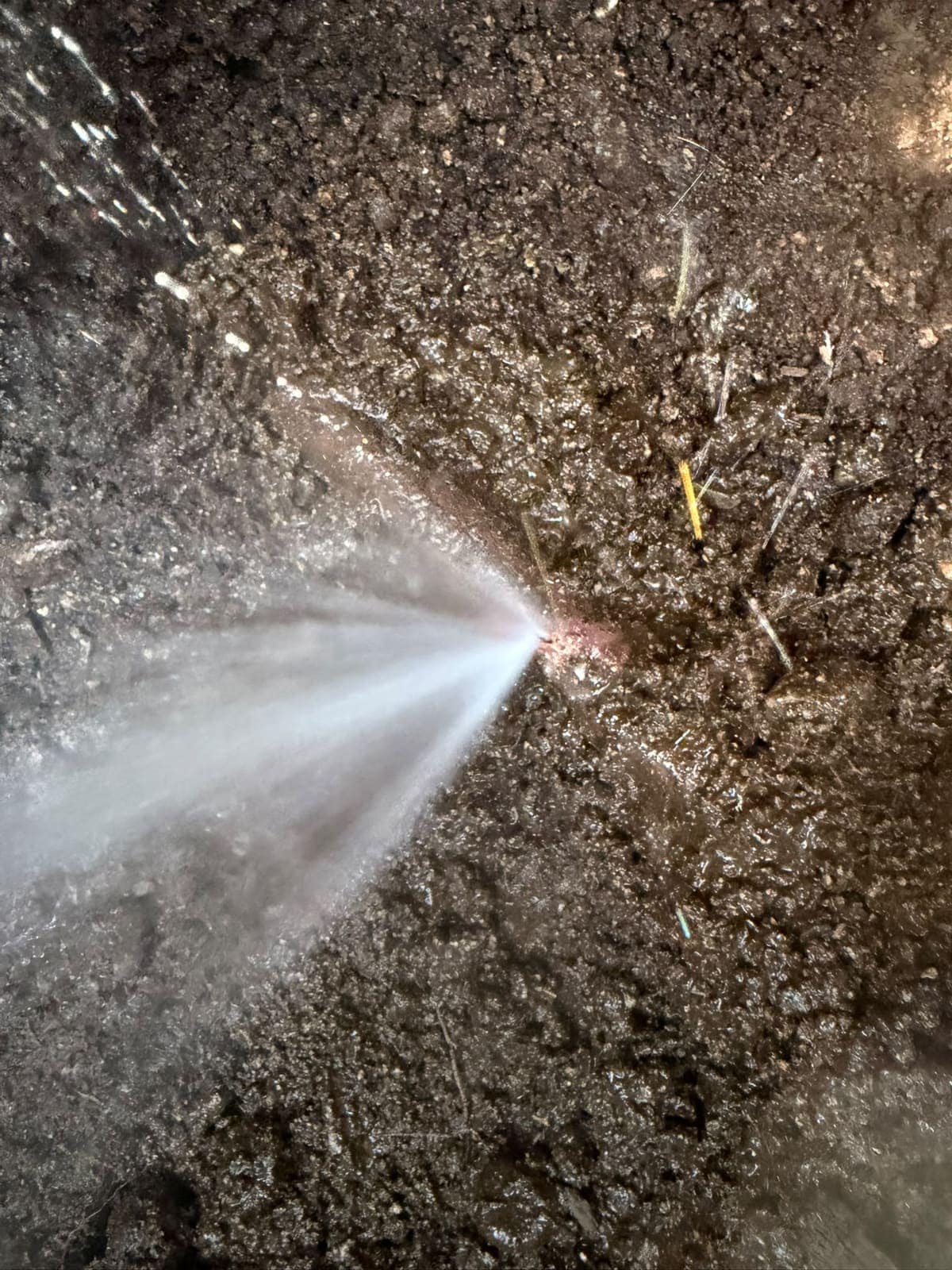 Pressurised pinhole leak spraying from a buried water line in an open excavation