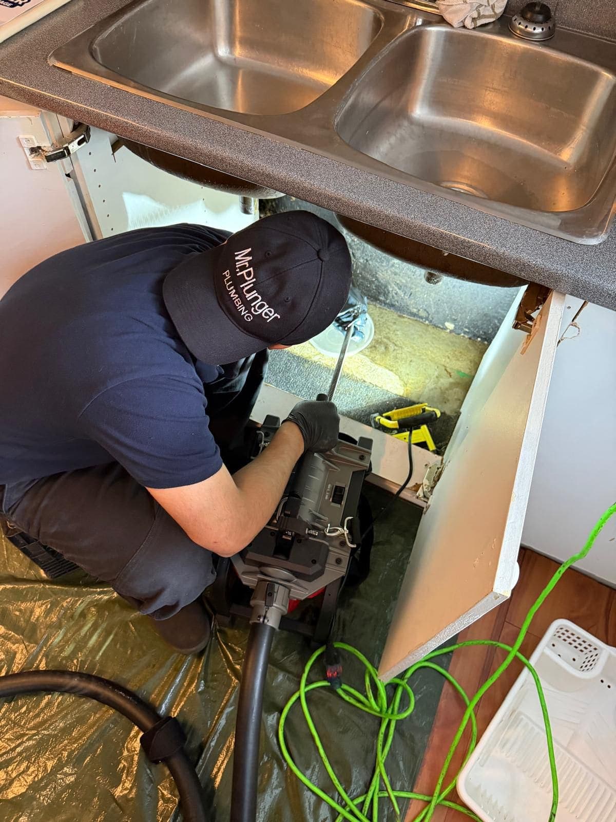 Mr. Plunger plumber unclogging a kitchen sink drain with a drum-fed cable machine