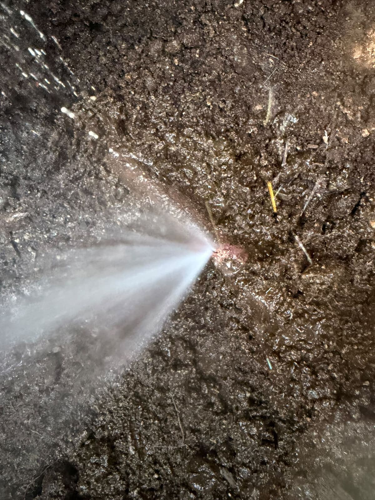 Pressurised pinhole leak spraying from a buried water line in an open excavation